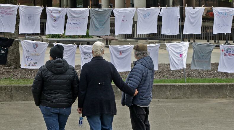 People look over the Clothesline Project in downtown Springfield Friday. The project, from the Victim Witness Division of the Clark County Prosecutors Office, features T-shirts hanging from a clothesline with messages from victims of violent crimes. Some victims wrote messages to the person who hurt them and others wrote inspirational messages to other victims. The project, which lasted Friday and Saturday, was meant to give victims a voice. BILL LACKEY/STAFF