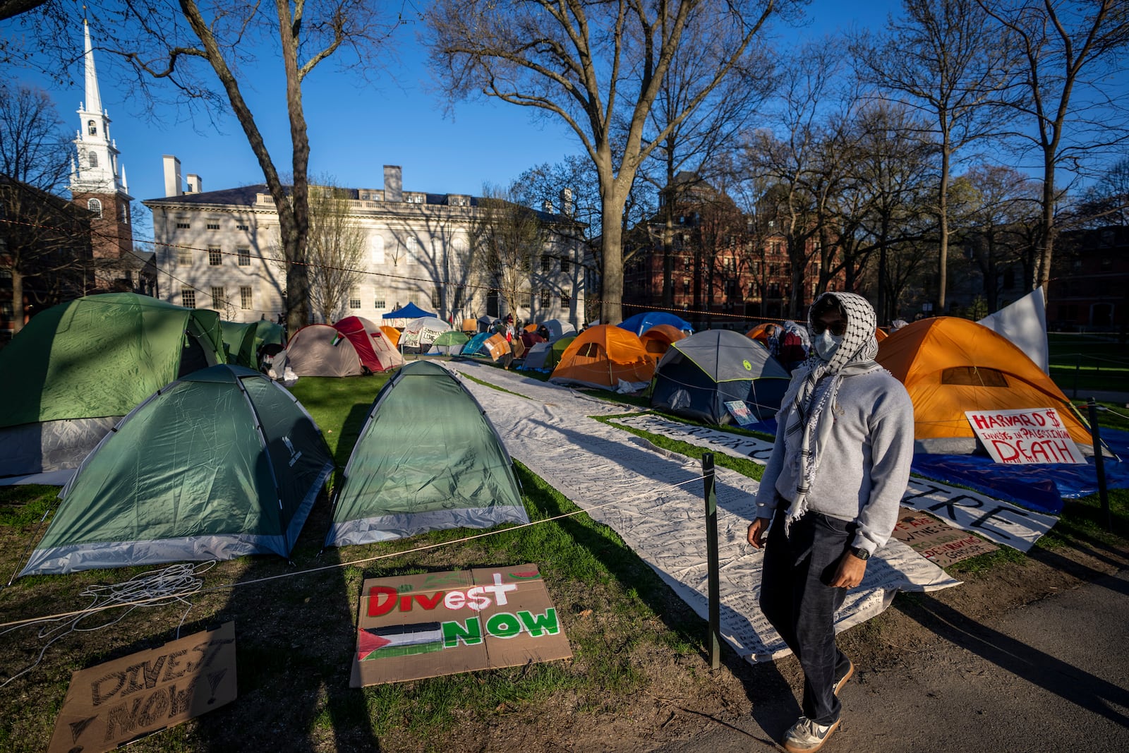 FILE - A student protester against the war in Gaza walks past tents and banners in an encampment in Harvard Yard, at Harvard University in Cambridge, Mass., on April 25, 2024. (AP Photo/Ben Curtis, file)