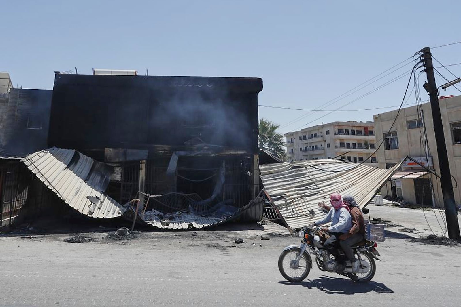 Syrian citizens ride in front of a shop that was burned during clashes between Syrian government forces and Druze militias on the outskirts of Sweida city, southern Syria, Wednesday, July 16, 2025. (AP Photo/Omar Sanadiki)