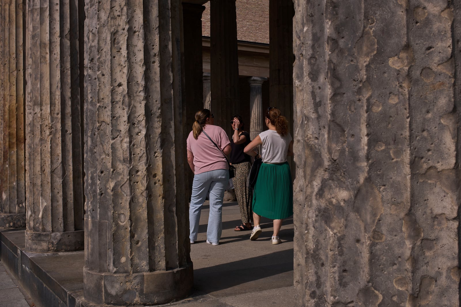 Tourists stand between the columns on Museum Island with holes from artillery fire from World War II, in Berlin, Germany, Friday, May 2, 2025. (AP Photo/Markus Schreiber)