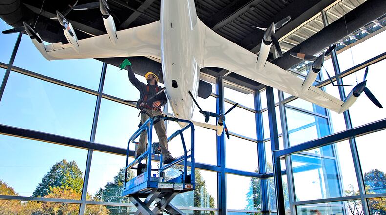Owen Flannery, an employee with the City of Springfield, cleans the electric vertical take off and landing aircraft that hangs in the lobby of the new National Advanced Air Mobility Center of Excellence at Springfield-Beckley Municipal Airport Thursday, Sept. 14, 2023. BILL LACKEY/STAFF