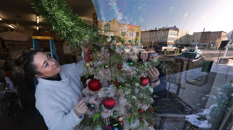 Downtown Urbana is reflected in the front window of the Vintage Traveler shop as owner, Tina Blakeman, and her friend Shannon Anderson decorate a Christmas tree in the window for the holidays earlier this month. BILL LACKEY/STAFF