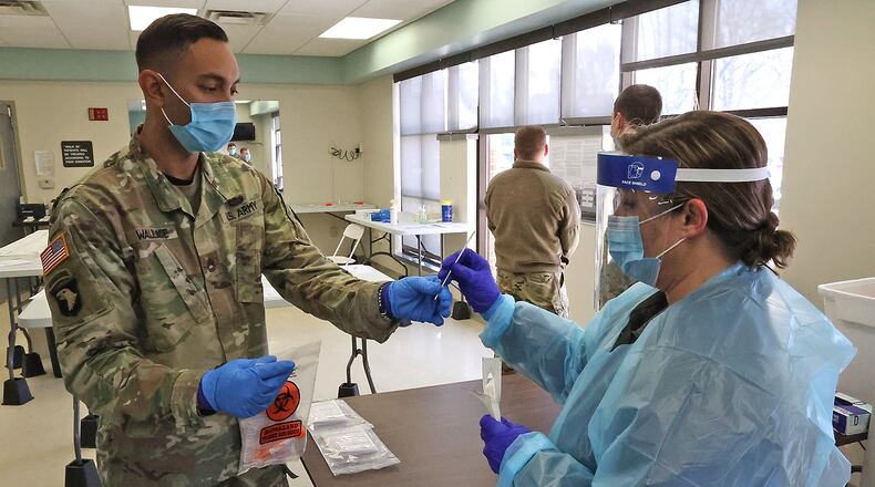 Renee Steele, from the Clark County Combined Health District, hands off a COVID test to SFC David Wallace of the Army National Guard so he can check it Tuesday at the COVID Testing Center on East High Street. BILL LACKEY/STAFF