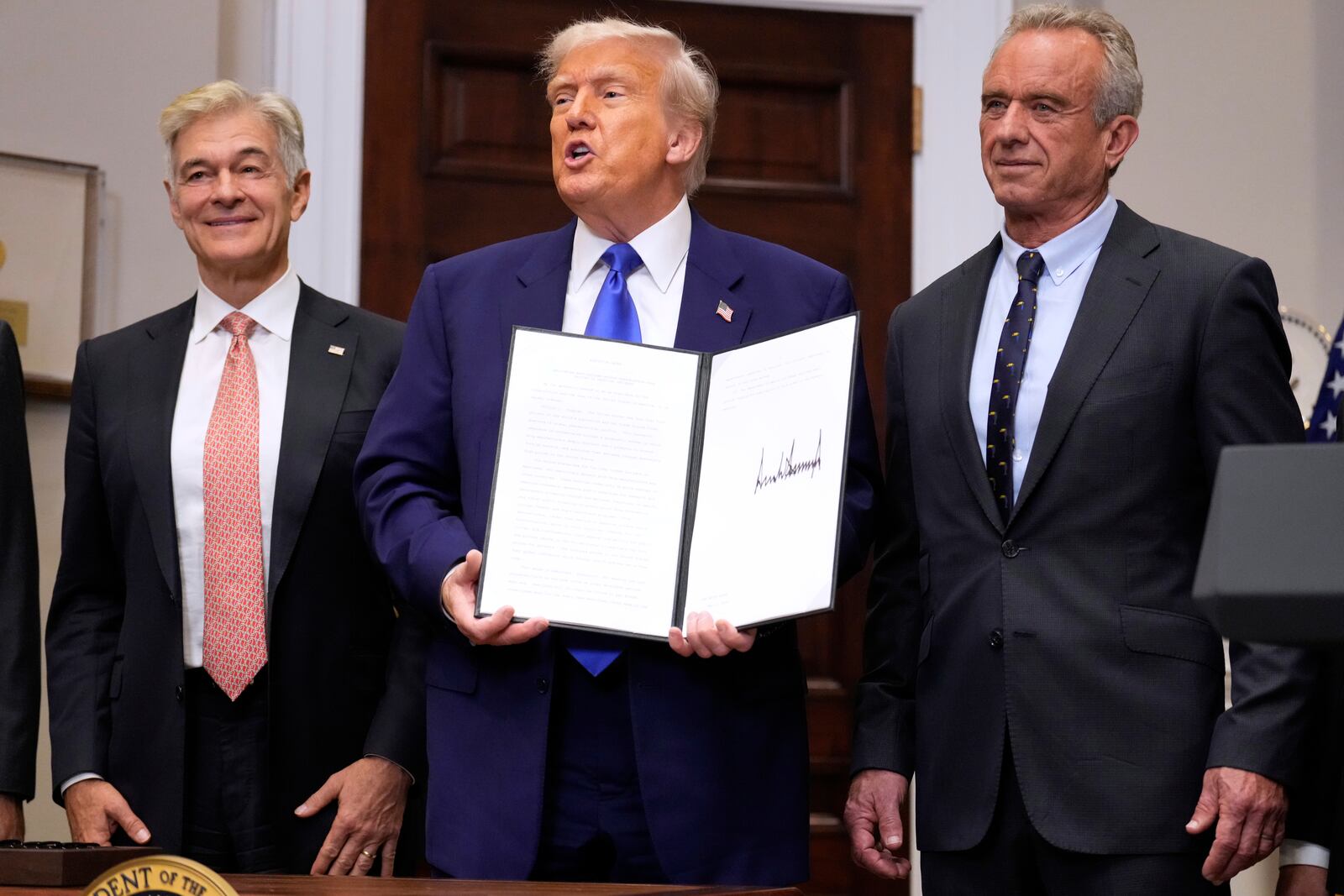 President Donald Trump, with Dr. Mehmet Oz, Administrator of the Centers for Medicare & Medicaid Services, left, and Health and Human Services Secretary Robert F. Kennedy Jr., right, holds an executive order related to drug prices, in the Roosevelt Room of the White House in Washington, Monday, May 12, 2025, in Washington. (AP Photo/Mark Schiefelbein)