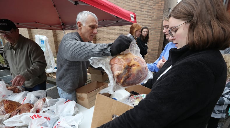 Volunteer Ed Jenkins puts hams in the food boxes which Caylee Hirtzinger, left, and Alyssa Blanke, from Shawnee High School, were filling up for a needy family at a previous St. Vincent de Paul Holiday Gift Basket distribution in Springfield. Bill Lackey/Staff
