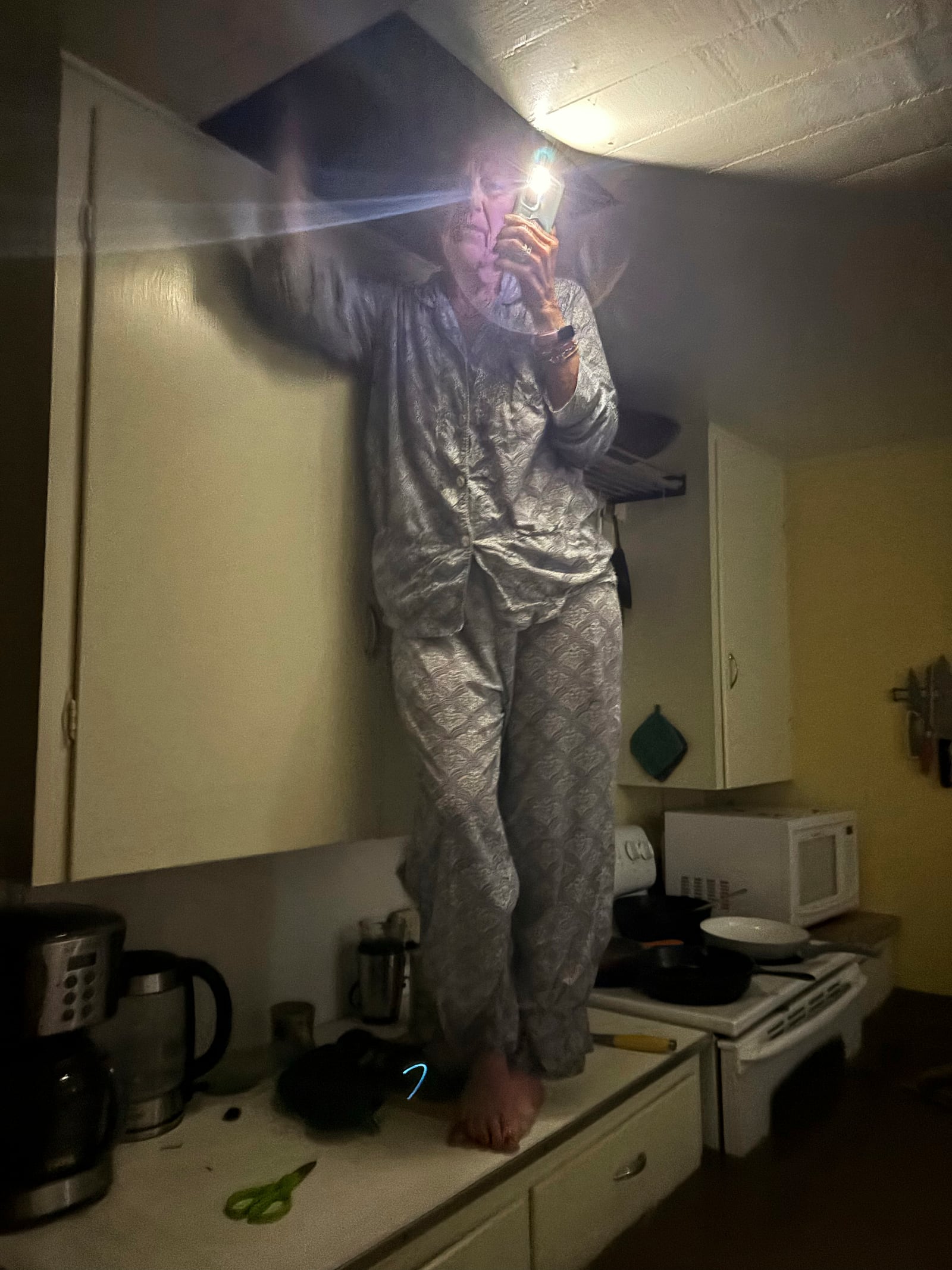 Jane Towler reaches into the attic as she stands on a kitchen countertop above floodwaters in the cabin of her son, Alden Towler, in Hunt, Texas, at 4:20 a.m. on Friday, July 4, 2025. (Shabd Simon-Alexander via AP)