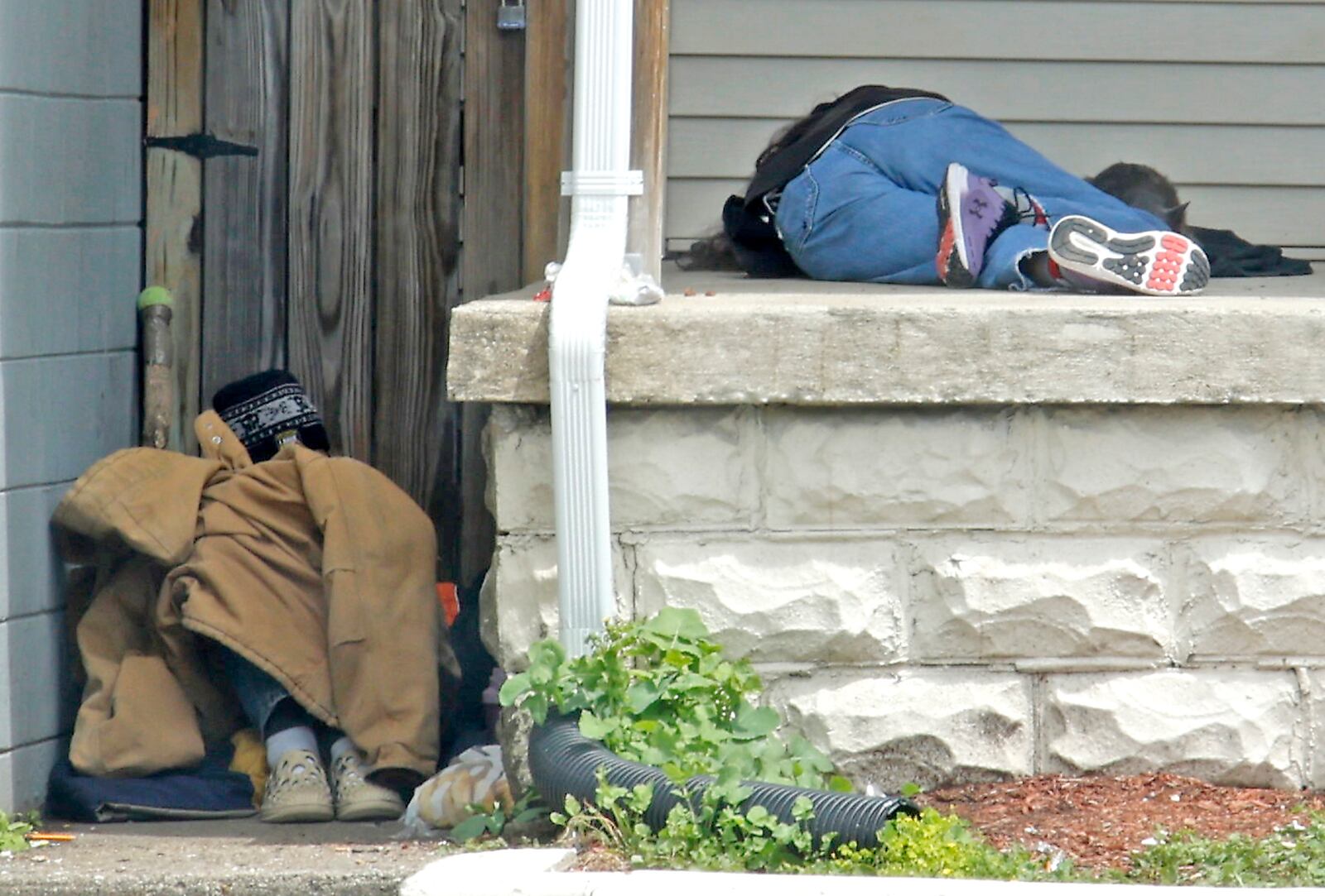 Several men sleep on the front porch of the Sheltered Inc. men's homeless shelter in May 2024 while the shelter, located along West High Street, closes during the day. BILL LACKEY/STAFF