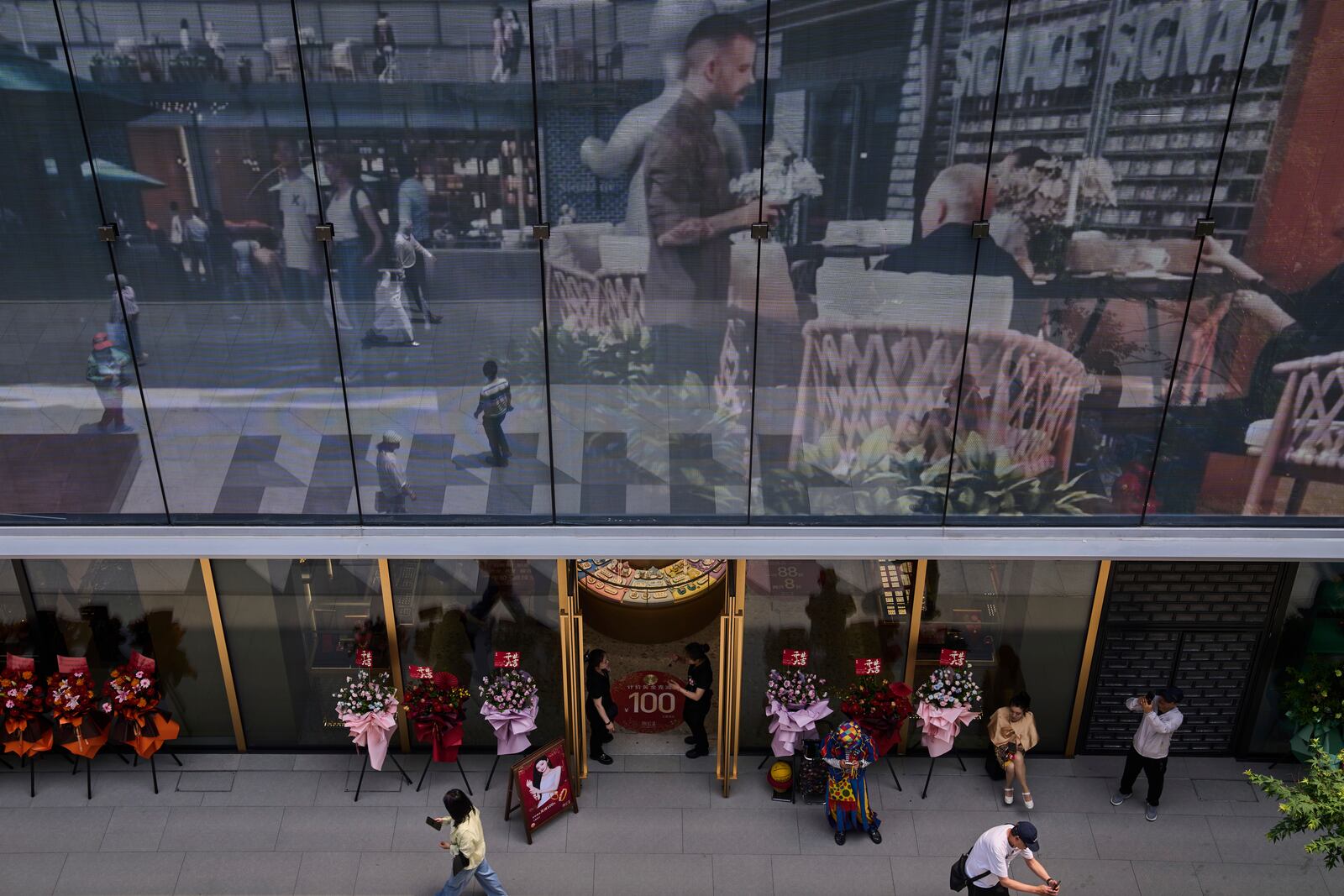 Workers wait for customer at a jewellry store as a projector screen promoting a newly opened outdoor Hutong style shopping mall, in Beijing, Monday, May 26, 2025. (AP Photo/Andy Wong)