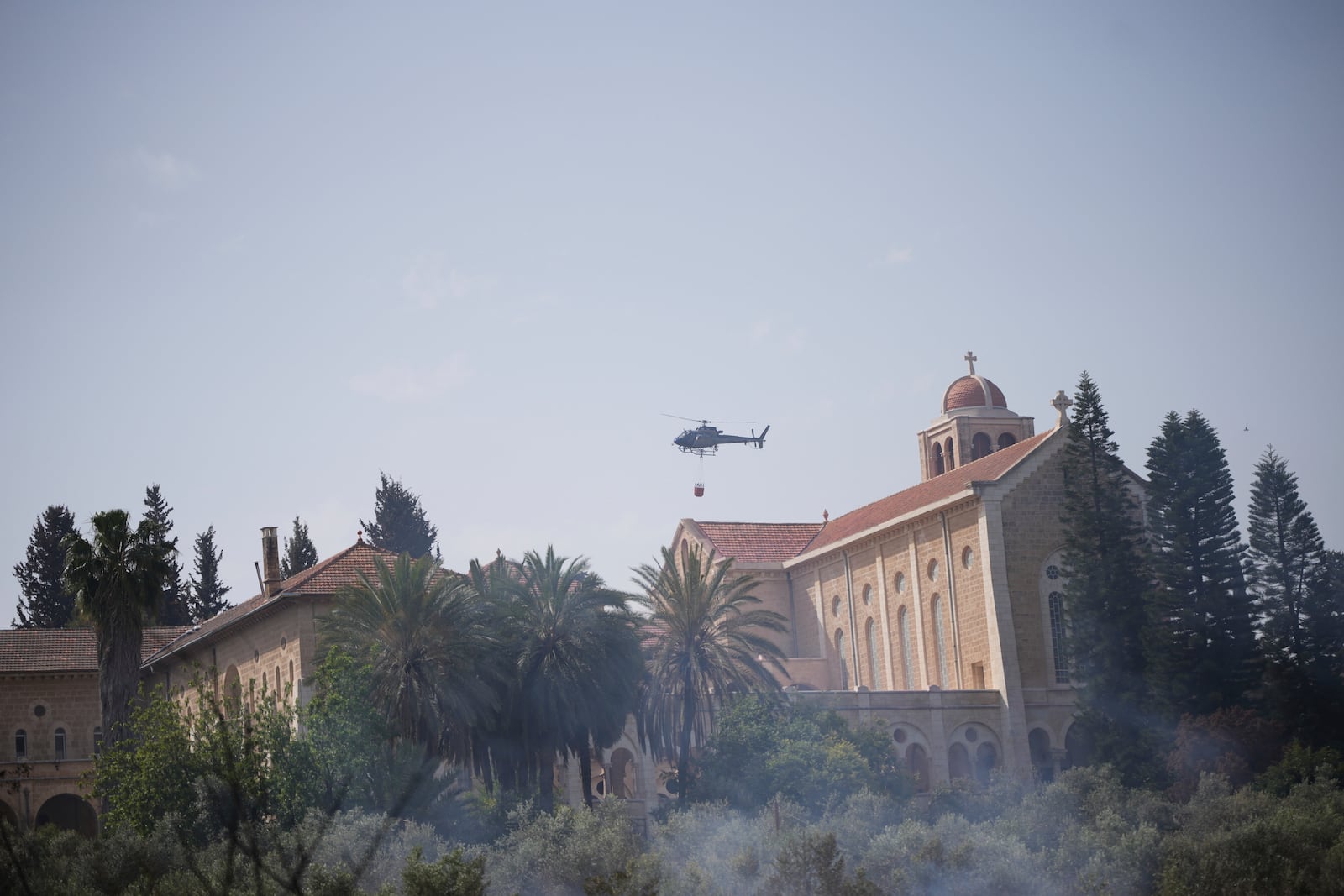 An Israeli fire helicopter flies over the Roman Catholic Trappist monastery where fire crew is battling a wild fire in Latrun, Israel, outside of Jerusalem Thursday, May 1, 2025. (AP Photo/Ohad Zwigenberg)