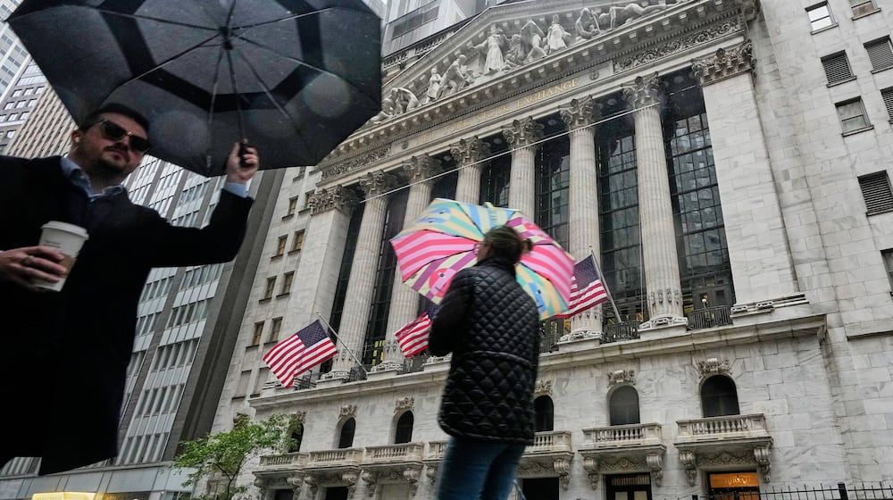 People with umbrellas pass the New York Stock Exchange, Monday, Oct. 13, 2025. (AP Photo/Richard Drew)