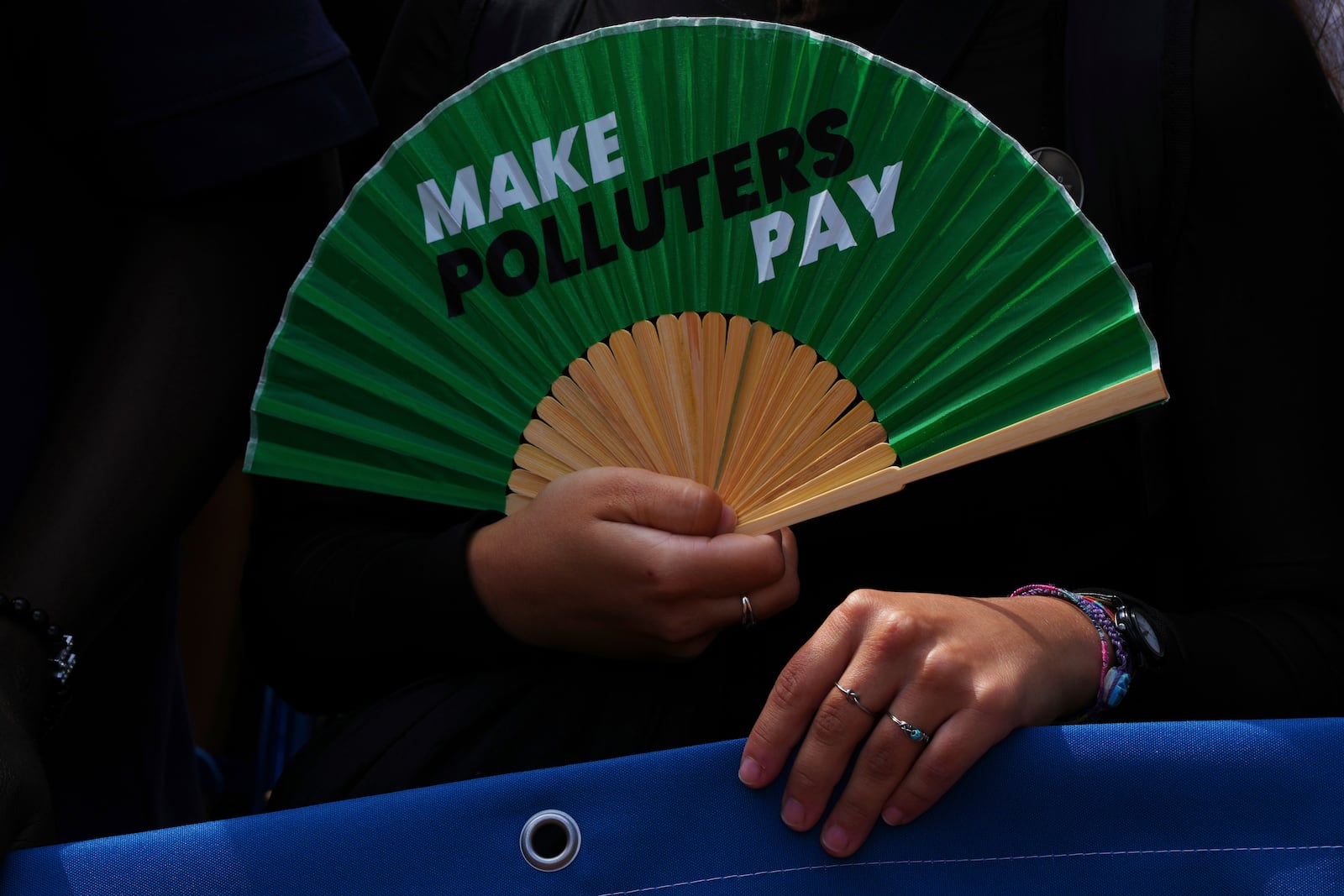 An activist holds a fan that reads "make polluters pay" as they demonstrate outside the International Court of Justice ahead of an advisory opinion on what legal obligations nations have to address climate change and what consequences they may face if they don't, Wednesday, July 23, 2025, in The Hague, Netherlands. (AP Photo/Peter Dejong)