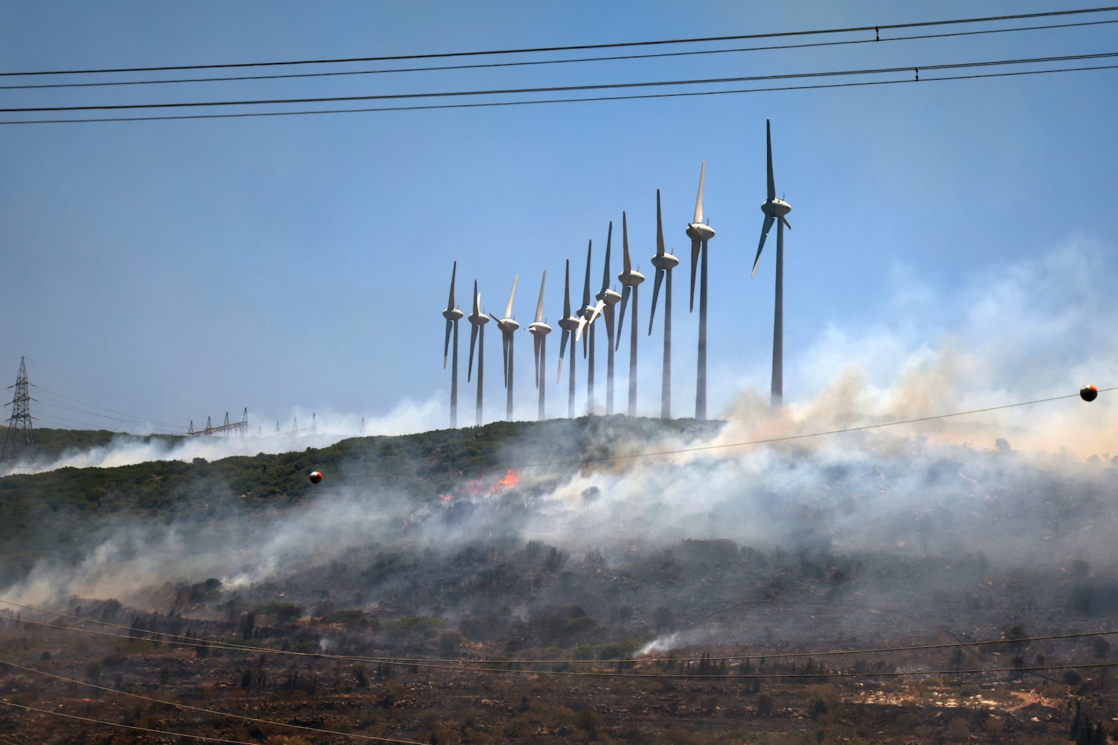 A fire rages near windmills in Cesme, near Izmir, Turkey, Thursday, July 3, 2025. (Cengiz Malgir/Dia Photo via AP)