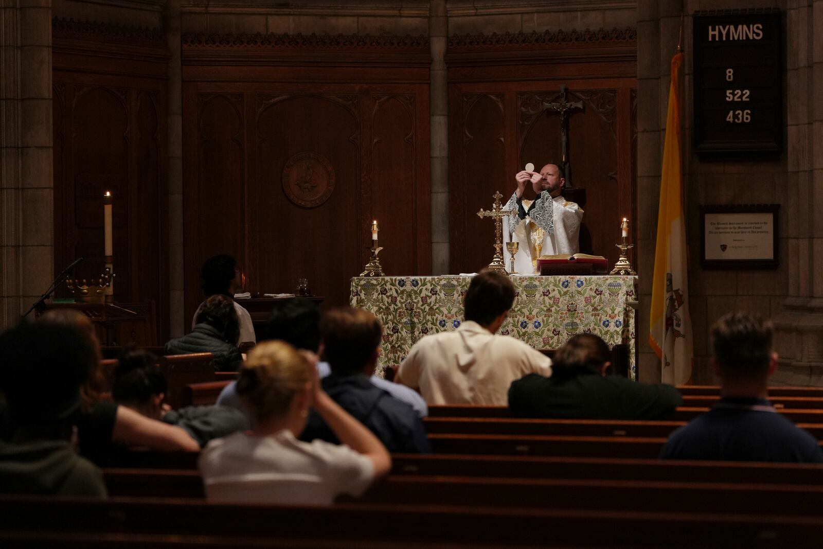 The Rev. Zachary Swantek, Princeton University’s Catholic chaplain and director of the Aquinas Institute - the university’s Catholic campus ministry - raises the host during the Eucharist at a side altar of the school's chapel during a Mass in Princeton, N.J., on Thursday, May 15, 2025. (AP Photo/Luis Andres Henao)