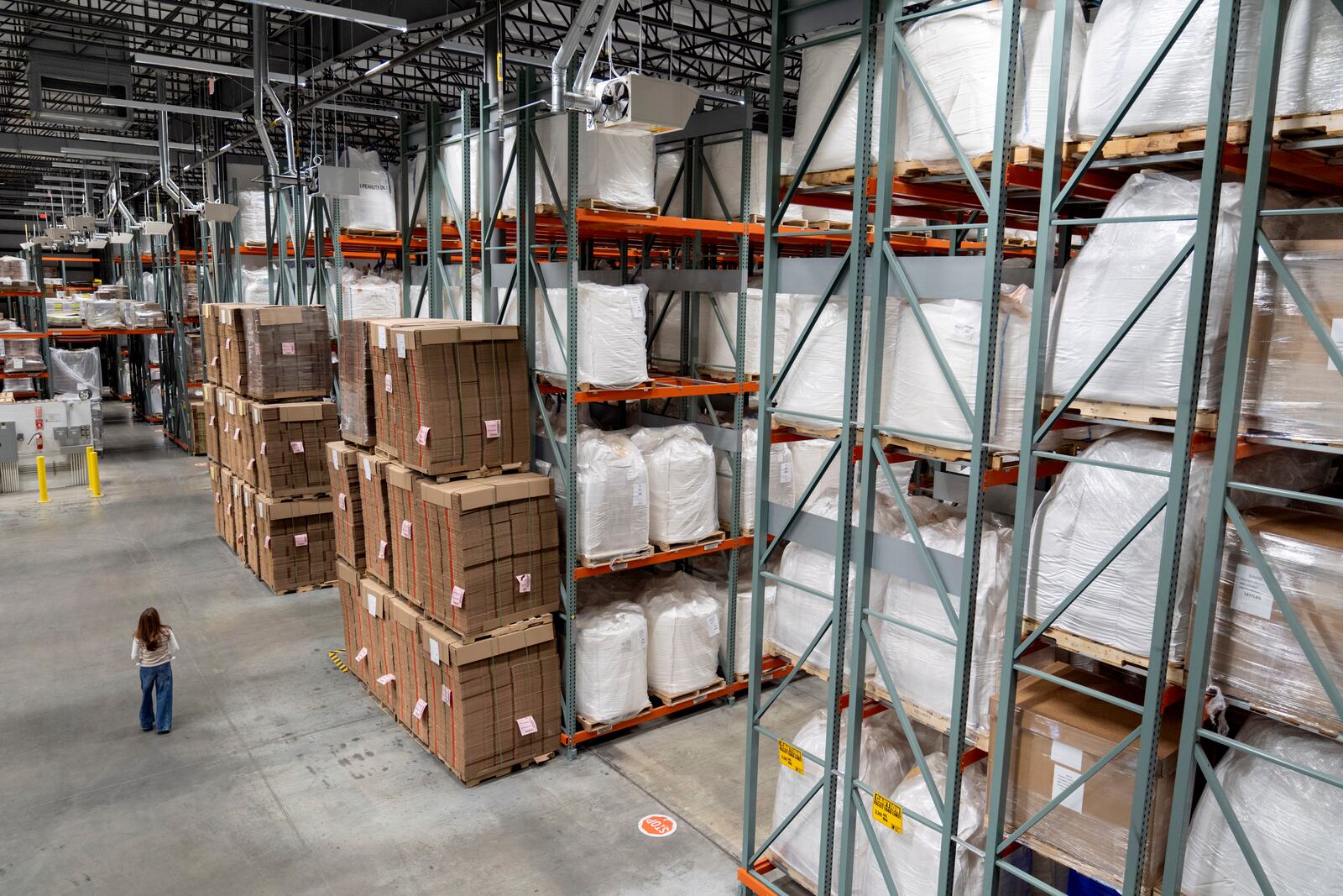 Edesia Nutrition CEO Navyn Salem walks past shipping boxes piled high alongside raw materials for Plumpy'Nut, a nutritional lifesaving peanut paste sent to malnourished children worldwide, at the company's warehouse Friday, March 14, 2025, in North Kingstown, R.I. (AP Photo/David Goldman)