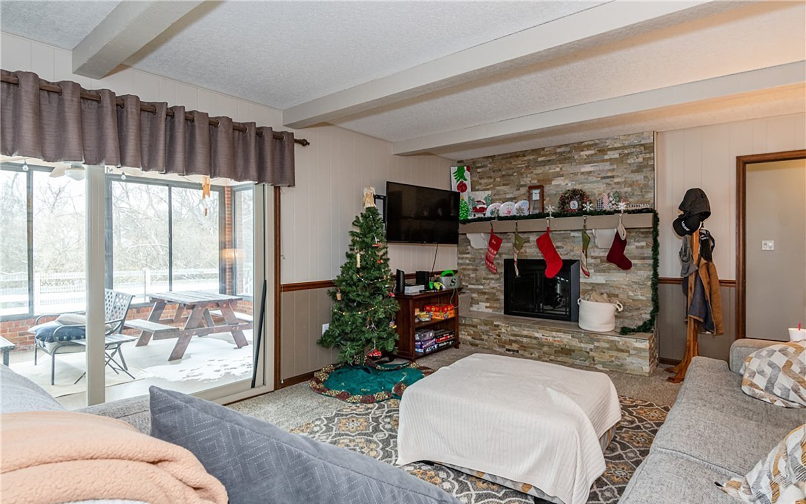 The family room has a stacked stone electric fireplace, carpeting, a beamed ceiling and wainscotting on the walls. CONTRIBUTED