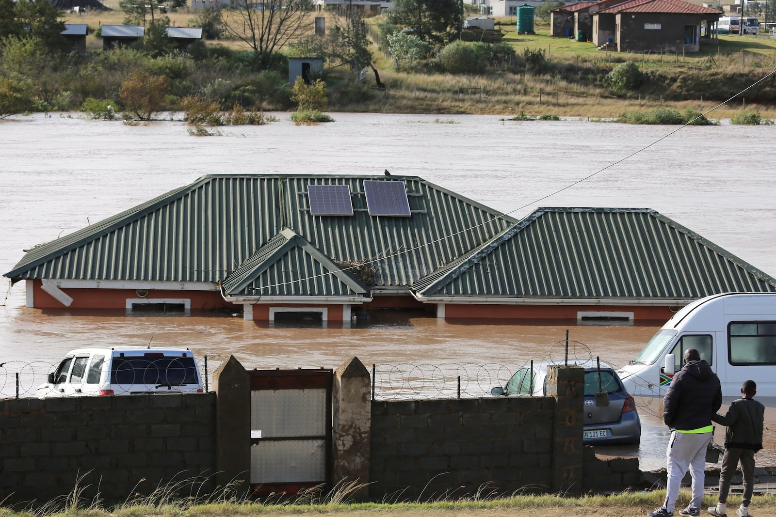 A man with a child look at a home submerged in floodwater, in Mthatha, South Africa, Tuesday, June 10, 2025. (AP Photo/Hoseya Jubase)