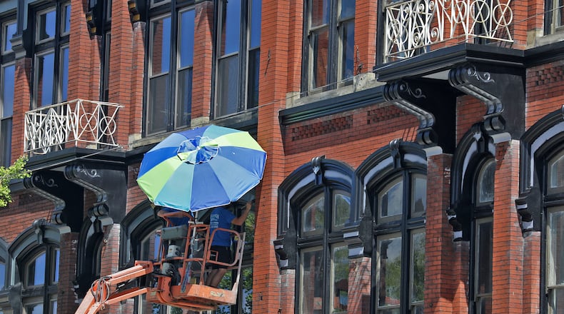 A painting crew uses a beach umbrella to provide a little shade while they paint the trim around windows of a building along North Main Street in Urbana in this August 2022 file image. The former Willman Furniture buildings will become a co-working and living space, in part because of state tax credits. BILL LACKEY/STAFF