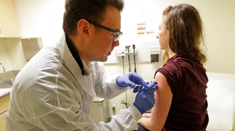 In this March 16, 2020, file photo, pharmacist Michael Witte, left, gives Rebecca Sirull a shot in the first-stage safety study clinical trial of a potential vaccine for COVID-19, the disease caused by the new coronavirus, Monday, March 16, 2020, at the Kaiser Permanente Washington Health Research Institute in Seattle. Sirull is the third patient to receive the shot in the study.