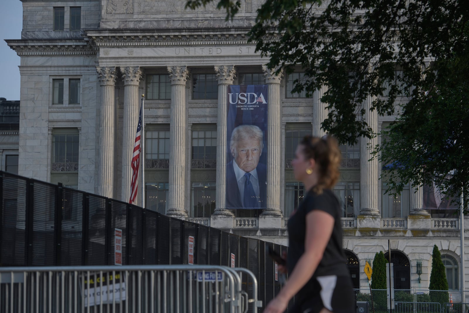 A woman walks past security fencing set up on the National Mall, during preparations for an upcoming military parade commemorating the Army's 250th anniversary and coinciding with President Donald Trump's 79th birthday, Thursday, June 12, 2025, in Washington. (AP Photo/Rod Lamkey, Jr.)