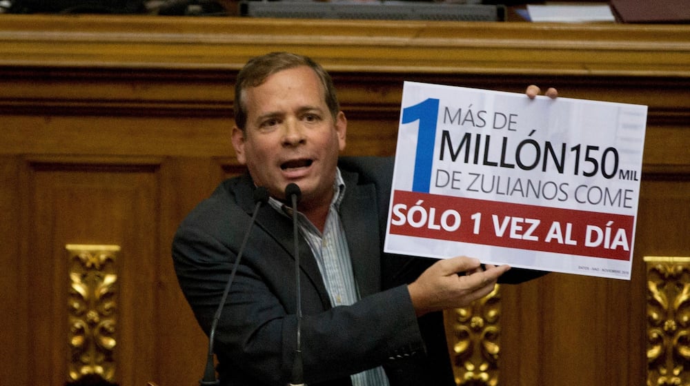 FILE - Opposition lawmaker Juan Pablo Guanipa displays a sign that reads in Spanish "More than a million residents of Zulia State eat only once a day" during an intervention against Venezuela's President Nicolas Maduro at National Assembly, in Caracas, Venezuela, Dec. 13, 2016. (AP Photo/Fernando Llano, File)