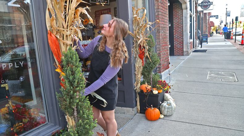 Mallory Janicki straightens the corn stalk and pumpkin decorations outside Champion City Guide and Supply Friday, Oct. 21, 2022 in downtown Springfield. BILL LACKEY/STAFF
