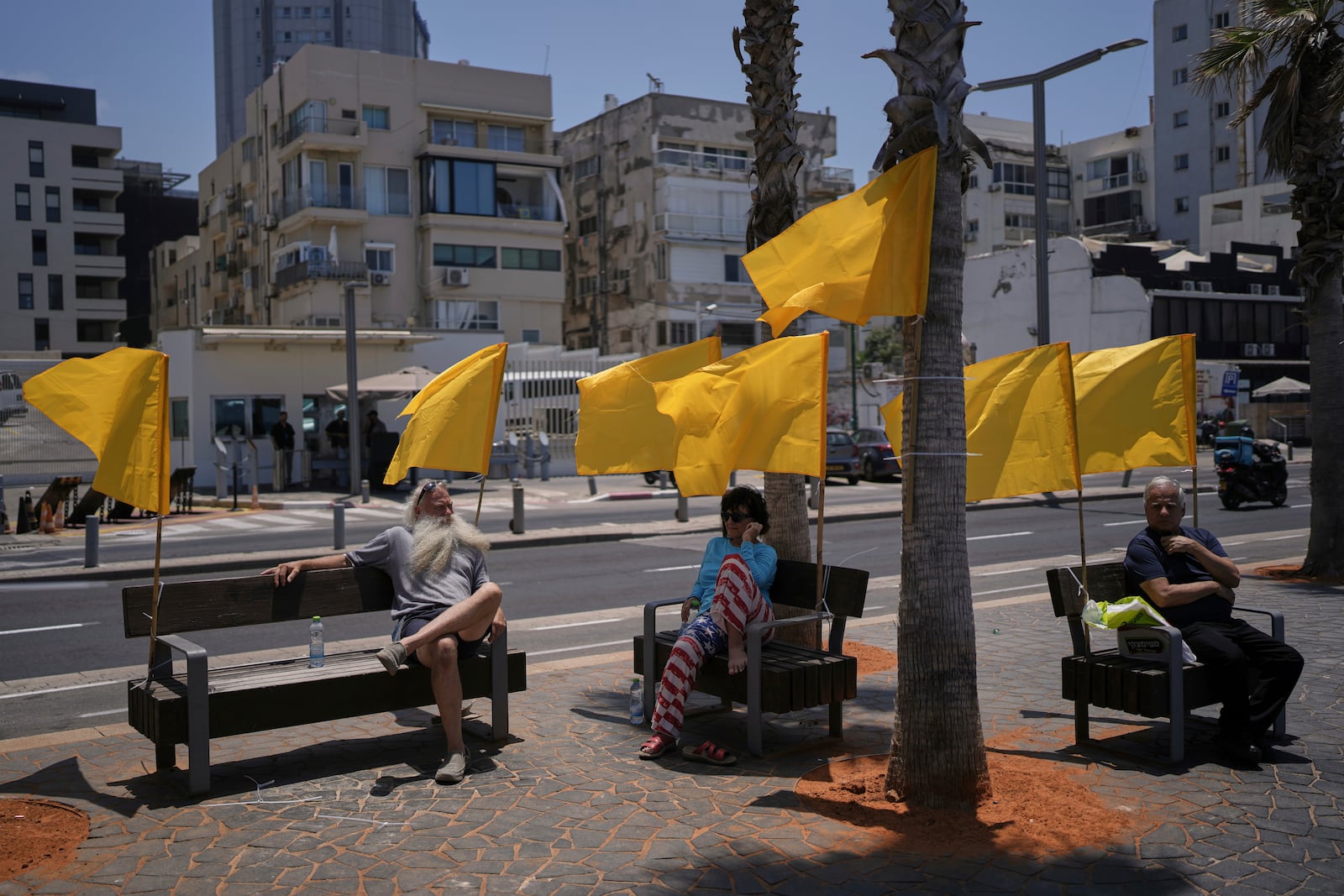 People sit on benches, decorated with yellow flags symbolizing the hostages being held by Hamas in the Gaza Strip, at the beachfront in Tel Aviv, Israel, Friday, July 4, 2025. (AP Photo/Oded Balilty)