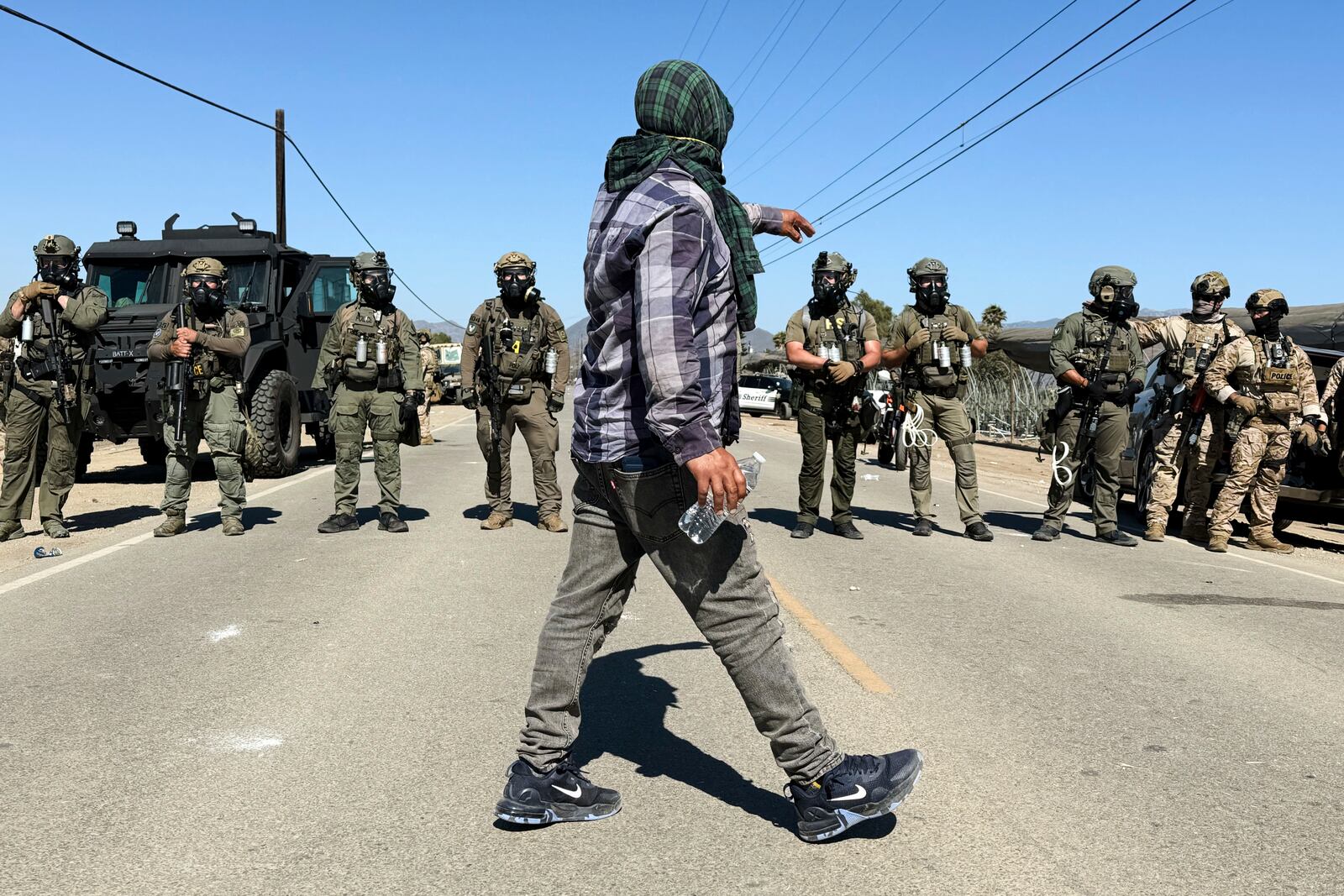 A demonstrator walks in front of federal agents blocking a road during an immigration raid in Camarillo, Calif. (AP Photo/Michael Owen Baker)