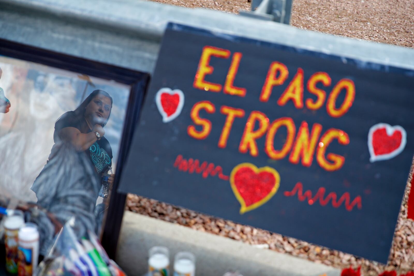 FILE - A woman is reflected in a picture as she looks at a makeshift memorial at the scene of a mass shooting at a shopping complex Tuesday, Aug. 6, 2019, in El Paso, Texas. (AP Photo/John Locher, File)