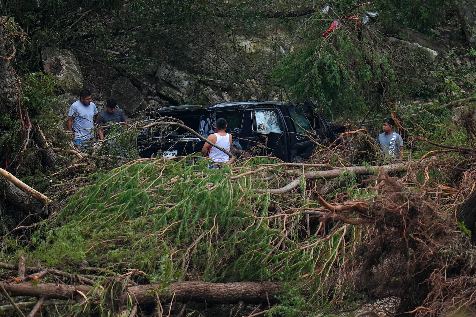 Men inspect a vehicle that was washed along the Guadalupe River near Camp Mystic after a flash flood swept through the area Saturday, July 5, 2025, in Hunt, Texas. (AP Photo/Julio Cortez)