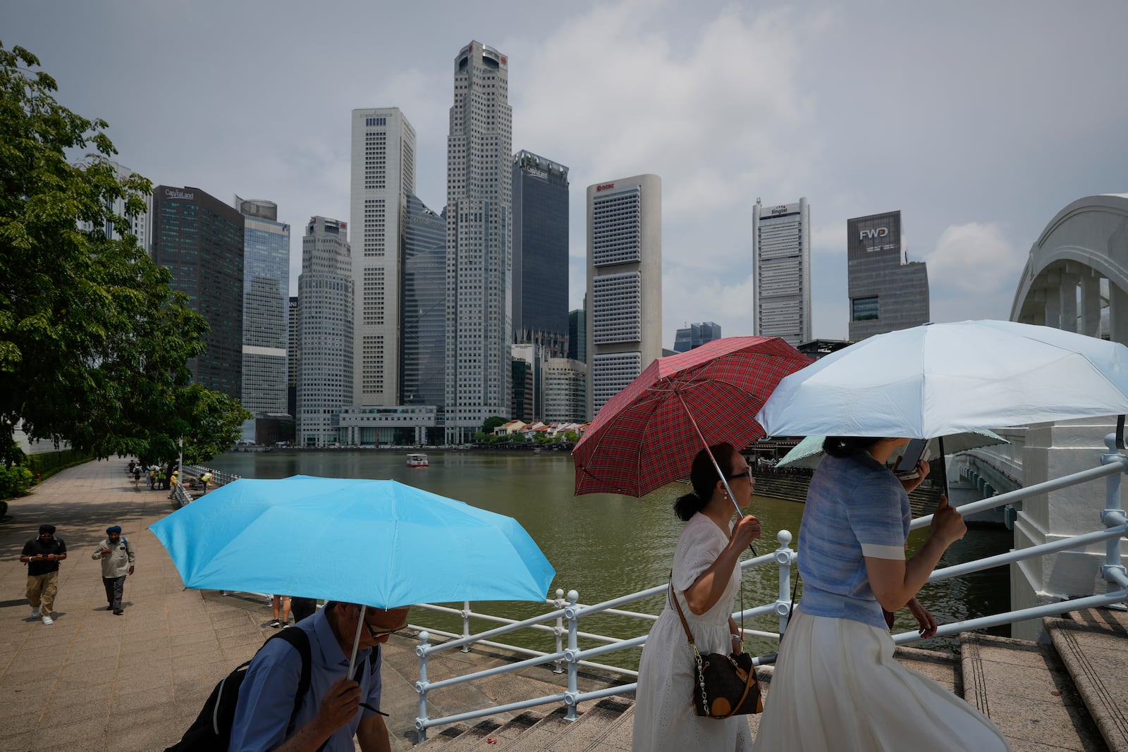 People walk with umbrellas, with the centre business district in the background, in Singapore, Friday, May 2, 2025. (AP Photo/Vincent Thian)
