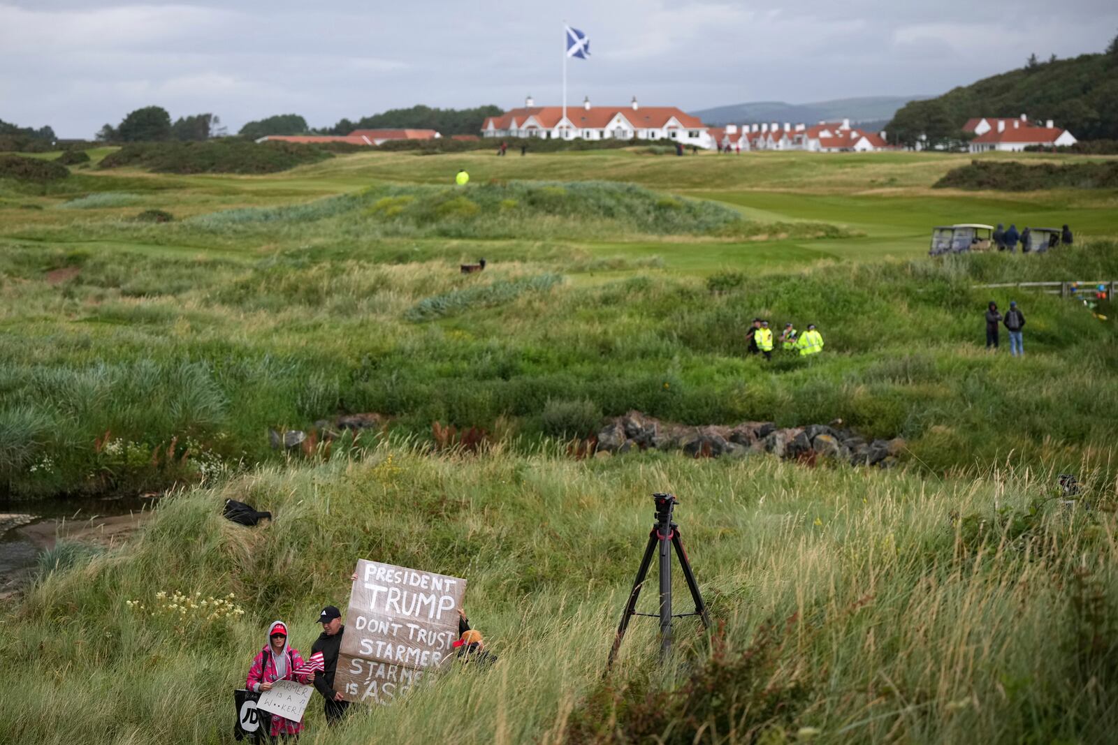 EDS NOTE: OBSCENITY - Trump supporters are watched by police and security forces as they hold signs near the Trump Turnberry golf course where President Donald Trump resides during his stay in Turnberry, Scotland, Sunday, July 27, 2025. (AP Photo/Alastair Grant)