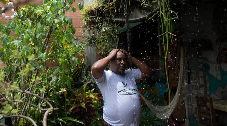 FILE - Luis Cassiano cools off with water that falls from his green roof at his home in Arara, a poor neighborhood, in Rio de Janeiro on Jan. 9, 2020. (AP Photo/Silvia Izquierdo, File)