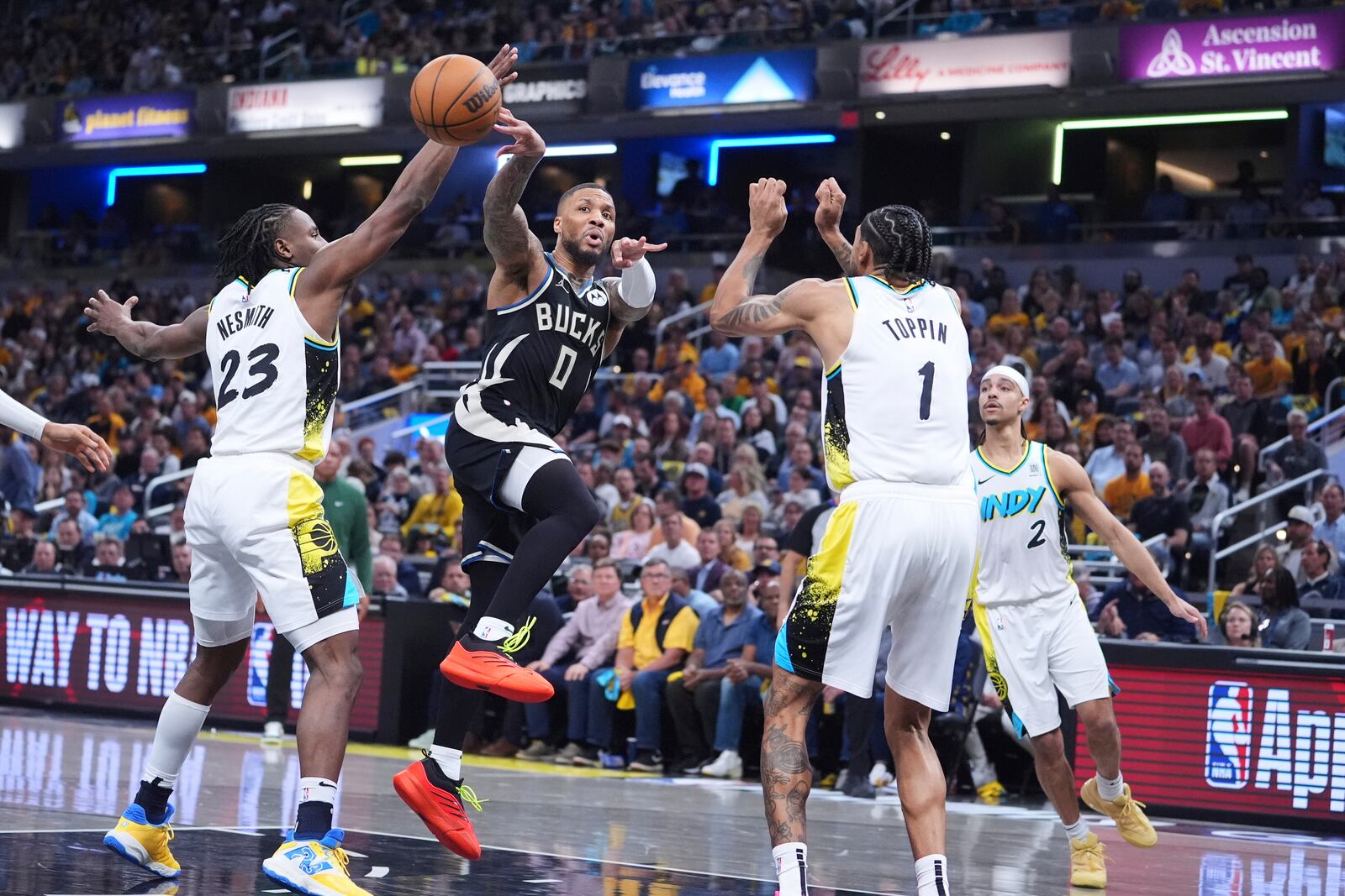 Milwaukee Bucks guard Damian Lillard (0) makes a pass between Indiana Pacers forward Aaron Nesmith (23) and forward Obi Toppin (1) during the first half of a first-round NBA basketball playoff game in Indianapolis, Tuesday, April 22, 2025. (AP Photo/Michael Conroy)