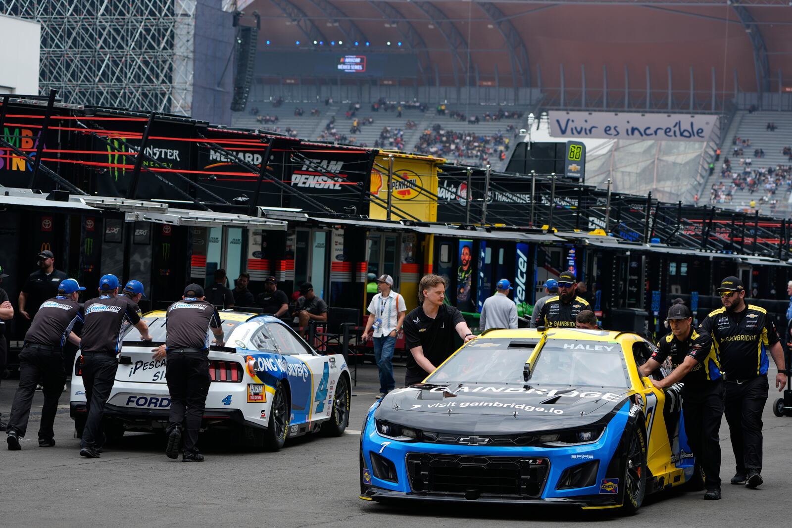 Mechanics of Justin Haley, right, and Noah Gragson push their cars on the paddock prior to a practice session for the NASCAR Cup Series auto race at the Hermanos Rodriguez race track in Mexico City, Friday, June 13, 2025. (AP Photo/Fernando Llano)