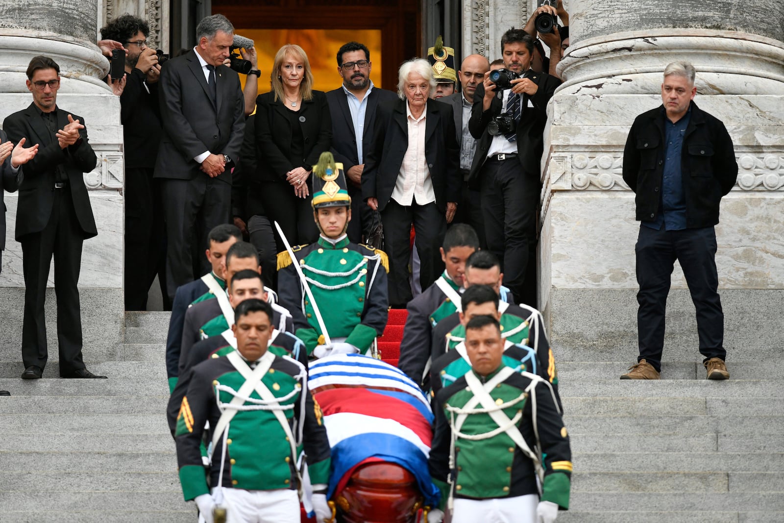 Uruguay's President Yamandu Orsi, back left, his wife Laura Alonsoperez, second from left, and Lucia Topolansky, the widow of late former President Jose Mujica, watch the honor guard carry his casket after funeral ceremonies at the Legislative Palace in Montevideo, Uruguay, Thursday, May 15, 2025. (AP Photo/Santiago Mazzarovich)