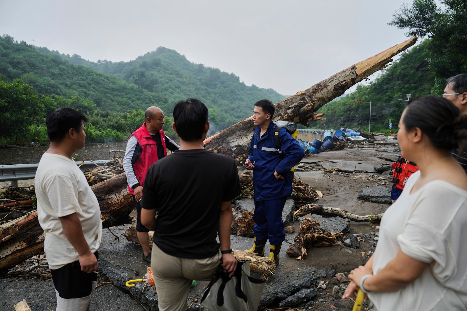 In this photo released by Xinhua News Agency, rescuers talk to villagers on a road damaged by floodwaters in Miyun District as continuous rain fall triggers alerts, in north of Beijing on July 27, 2025. (Ju Huanzong/Xinhua via AP)
