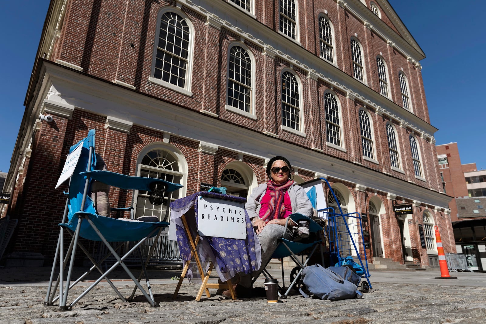 FILE - A fortune teller going by the name of Andrea waits for customers in front of Faneuil Hall in Boston, on a plaza that is usually busy with tourists, March, 14, 2020. (AP Photo/Michael Dwyer, File)