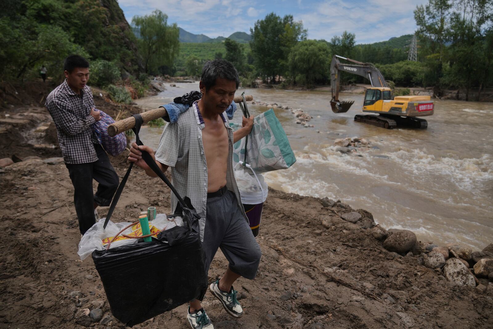 Villagers carrying belongings walk on a road damaged by flood as they evacuate from the Langjiayu village after heavy rains in Miyun district on the outskirts of Beijing, Tuesday, July 29, 2025. (AP Photo/Andy Wong)