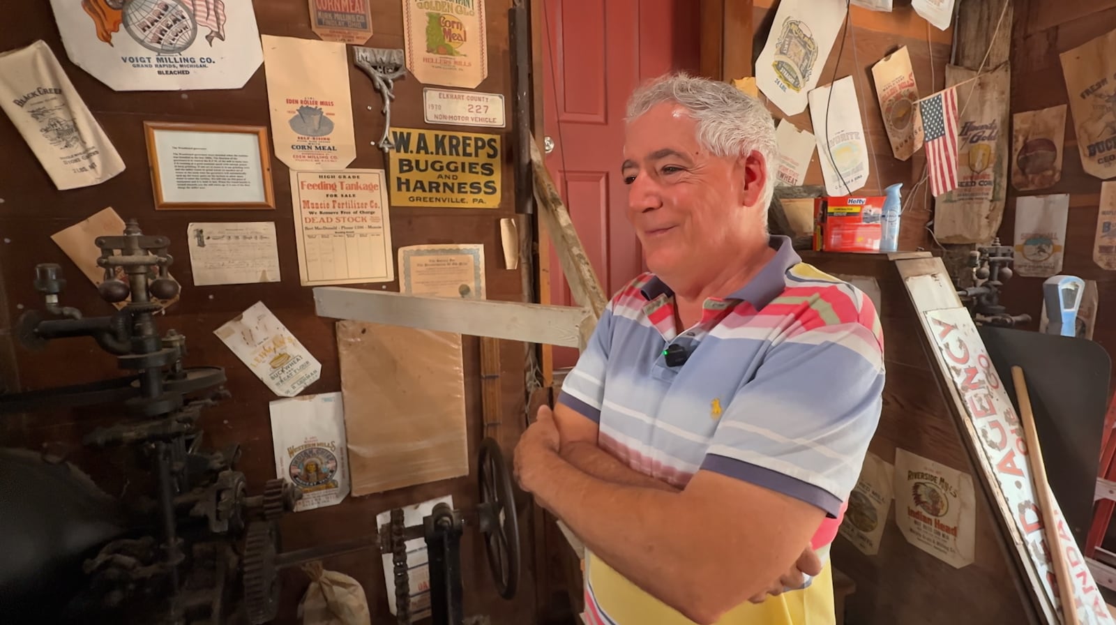 Anthony Satariano, wearing a striped polo shirt, stands with arms crossed inside the Historic Clifton Mill, speaking about his love for the village and its history.