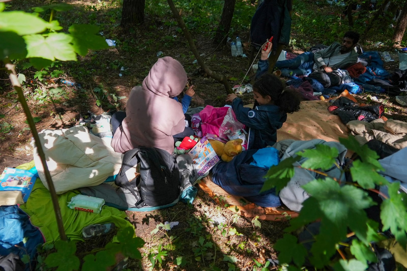Anouar, from Yemen, holds her daughter Kadi, 4, while her second daughter Jori, 6, center, right, and husband Qassim, from Palestine, right, wait in the forest of Ecault, northern France, Thursday, July 3, 2025. (AP Photo/Nicolas Garriga)