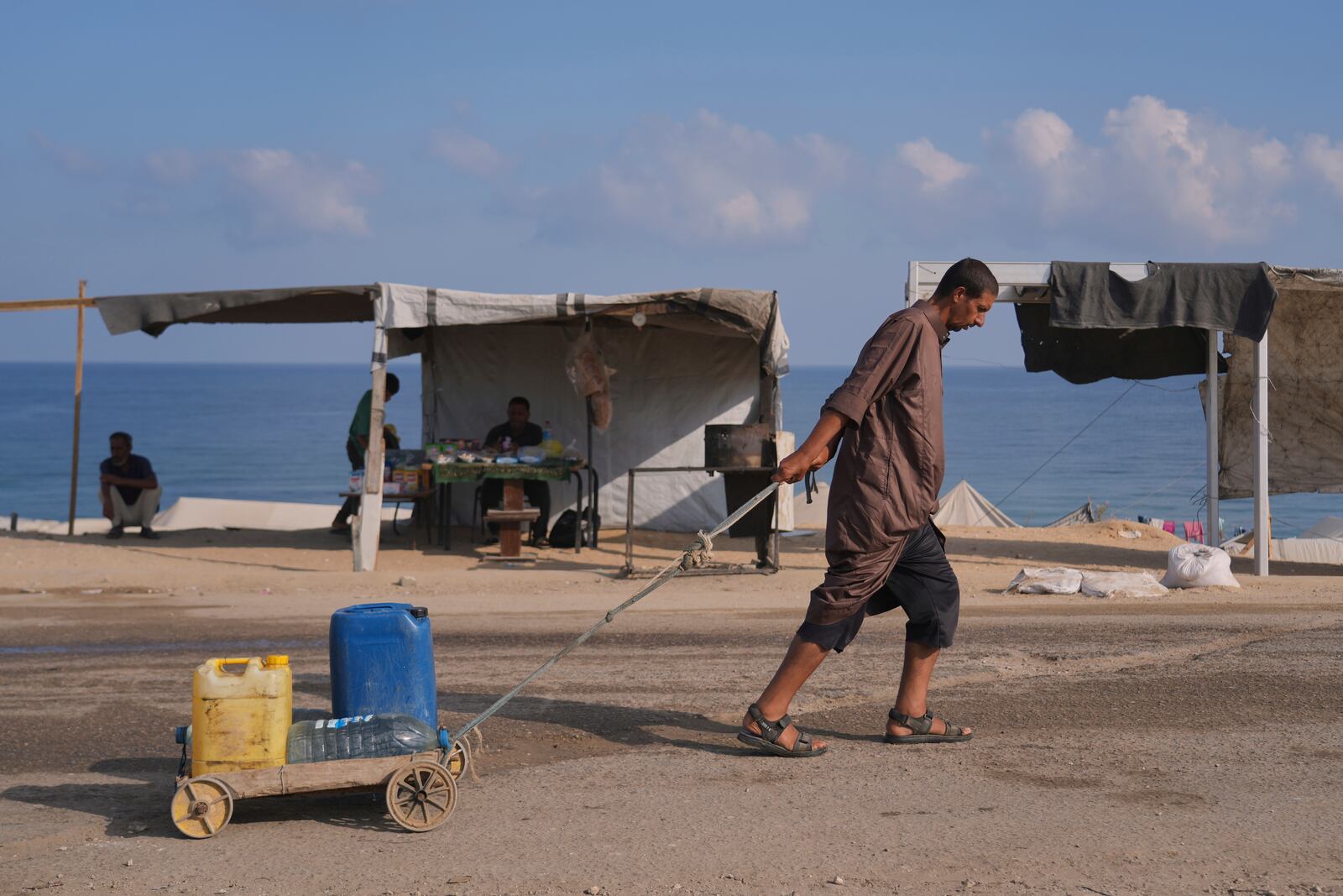 A man pulls a cart loaded with jerrycans and plastic bottles with water after collecting it at a camp for displaced people in Deir al-Balah, central Gaza Strip, Saturday, July 19, 2025. (AP Photo/Abdel Kareem Hana)