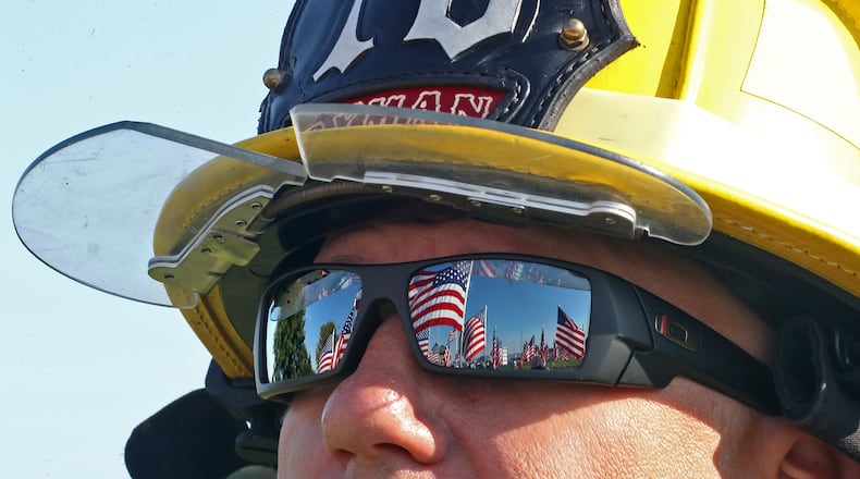 The field of American flags is reflected in the sunglasses of Fire Fighter Nathan Ryman, of the Rosewood Fire Department, Saturday during a 9/11 Remembrance Ceremony at Freedom Grove in Urbana. BILL LACKEY/STAFF