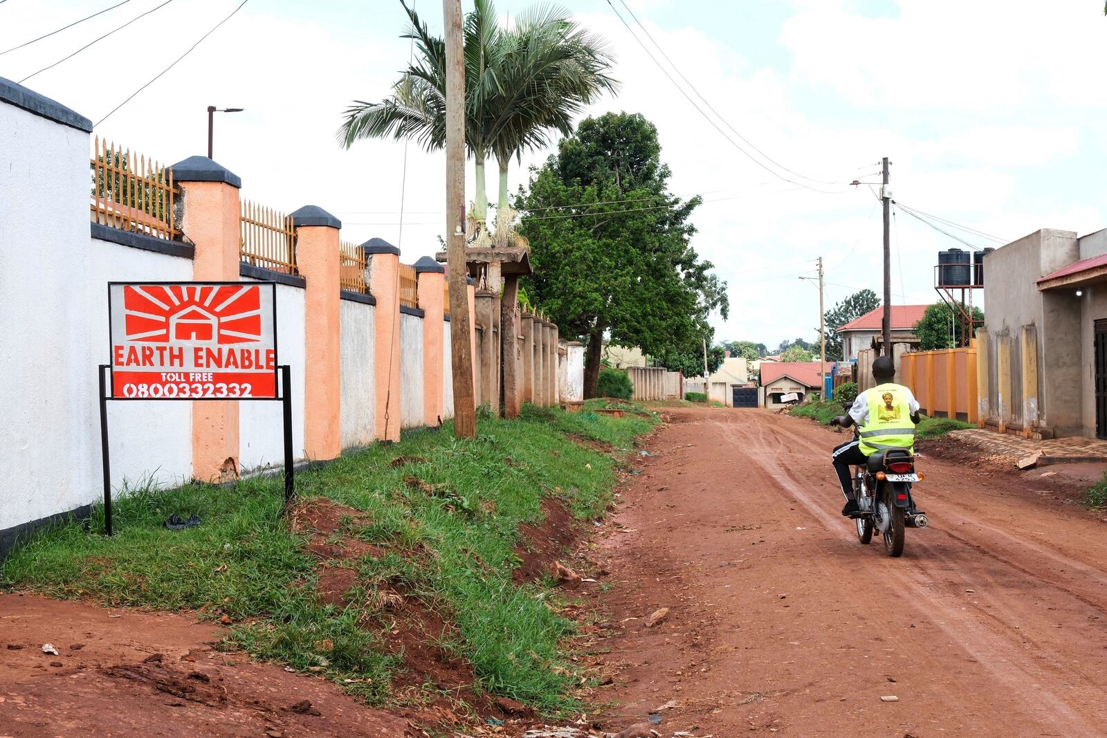 A person rides past a sign for EarthEnable on May 17, 2025, in Jinja, Uganda. (AP Photo/Hajarah Nalwadda)