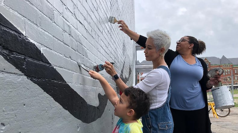 Braylon Bettinger, age 4, his grandmother Jessica Bettinger and Amber Vanderpool were part of a group of volunteers who gathered to paint a new mural on the back of the State Theater in downtown Springfield on Thursday morning. The mural sight was a filming location for an ABC Disney pilot being shot here, and Disney worked with the Springfield Public Arts Committee to create the mural here.