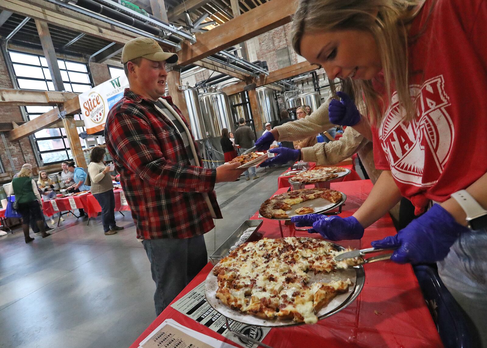 Maddie Myers, from Station 1, serves up a piece of pizza during the Slice of Springfield fundraiser at Mother Stewart's Brewery Thursday. Hundreds of people showed up for the second annual Slice of Springfield to sample pizza from eight area pizza shops and vote for their favorite while  raise money for a great cause. The Slice of Springfield fundraiser donated 100% of proceeds from ticket sales to help support National Trail Parks and Recreation. BILL LACKEY/STAFF