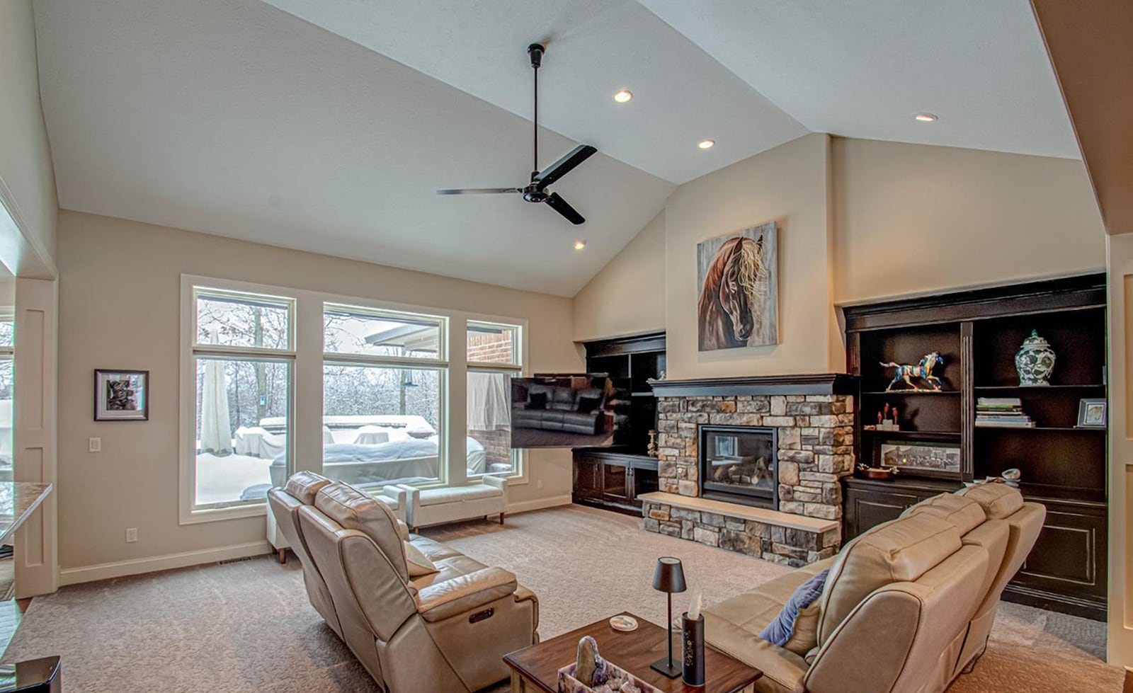 the living room has carpeting, a vaulted ceiling, recessed lighting and a ceiling fan. There is a stacked stone gas fireplace with a raised hearth and built in bookcases. CONTRIBUTED