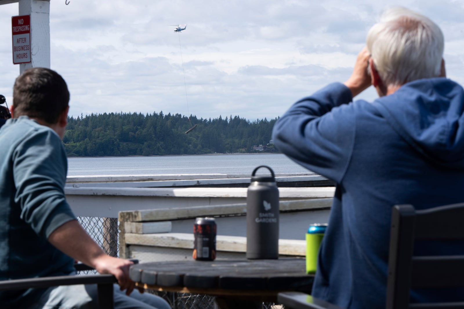 People watch as a helicopter carries an abandoned ship from Squaxin Island to shore on Wednesday, June 4, 2025, in Olympia, Wash. (AP Photo/Jenny Kane)
