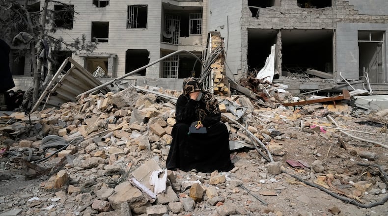 A woman sits on rubble across from a residential building damaged last Monday during the U.S.-Israeli air campaign in Tehran, Iran, Thursday, March 12, 2026. (AP Photo/Vahid Salemi)