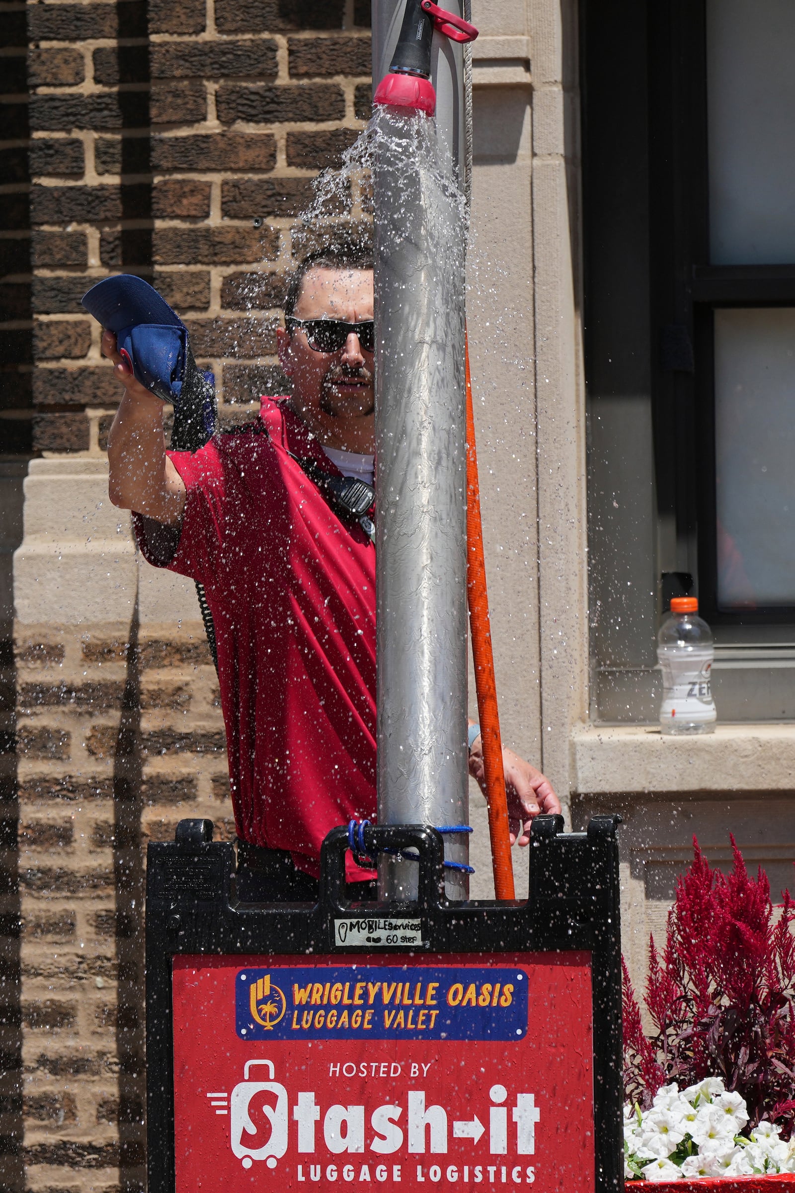 A Chicago Cubs security guard cools off under a sprinkler provided by a Chicago Fire Department outside of Wrigley Field before a baseball game between the Seattle Mariners and the Chicago Cubs in Chicago, Sunday, June 22, 2025. (AP Photo/Nam Y. Huh)
