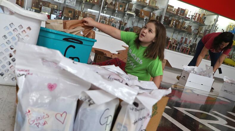 Triad Schools Superindent Vickie Hoffman, left, sits with Emma Bialecki and her mother, Heather, with some of the 900 care sacks they made up to be distributed with food this Sunday. BILL LACKEY/STAFF